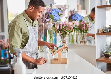 Smiling Handsome Male Is Using POS Terminal And Tablet For Selling Flower Bouquets In Shop