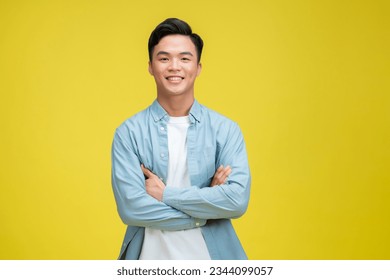 Smiling handsome man in blue polo shirt standing with crossed arms isolated on yellow background - Powered by Shutterstock
