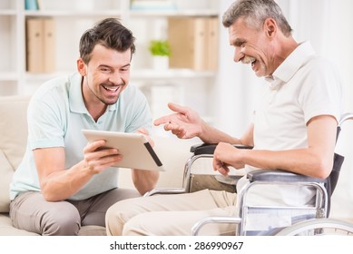 Smiling handsome man taking care about his eldery father in wheelchair. - Powered by Shutterstock