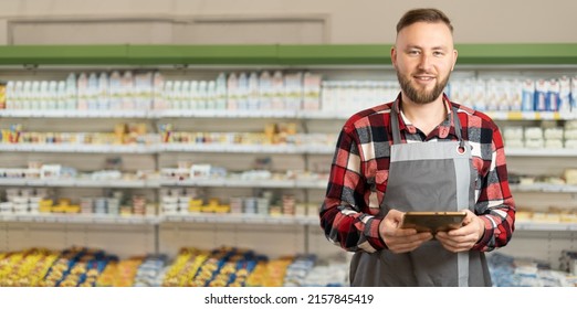 Smiling Handsome Man Using A Digital Tablet At Supermarket, Portrait Of Happy Caucasian Male Worker Standing In Supermarket And Typing On Tablet. Retail Concept. Banner, Place For Text