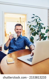 Smiling Handsome Man Working On Laptop At Home Drinking Coffee