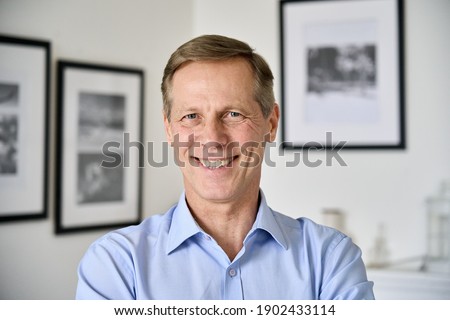 Smiling handsome middle aged 50s single man looking at camera standing at home, happy satisfied confident senior mature european male model posing indoors for close up face headshot portrait.