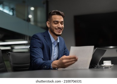 Smiling Handsome Middle Eastern Businessman In Expensive Suit Checking Reports In Modern Office, Satisfied By Results Of His Company, Sitting At Worktable In Front Of Laptop, Copy Space