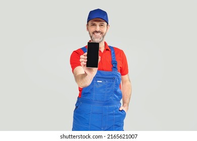 Smiling Handsome Plumber, Repairman Looking At Camera, Smiling And Holding Mobile Phone With Empty Screen. Handyman. A Lot Of Copy Space.
