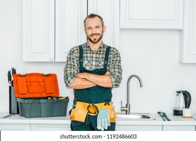 smiling handsome plumber standing with crossed arms and looking at camera in kitchen - Shutterstock ID 1192486603