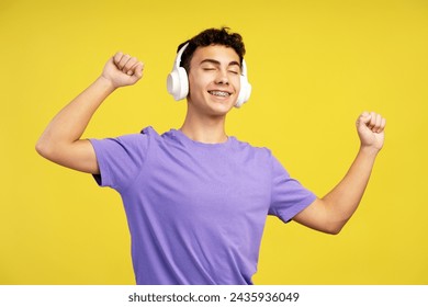 Smiling handsome teen boy with braces listening to music in headphones dancing with closed eyes having fun isolated on yellow background. Technology concept - Powered by Shutterstock