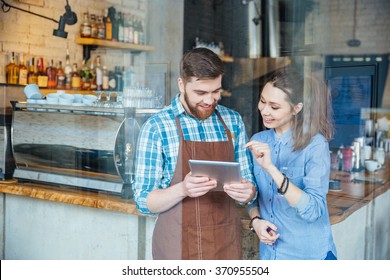 Smiling handsome waiter holding tablet and young pretty woman pointing on it in coffee shop