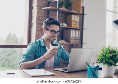 Smiling handsome worker in glasses drinking coffee while watching video on his laptop at office