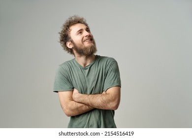 Smiling Handsome Young Man With Bearded And Wild Curly Hair, Bright Blue Eyes Looking Up With Hands Folded Isolated On White Background. Young Thinking Man In Green T-shirt On White Background. 