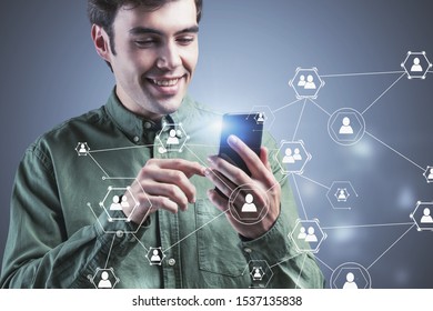 Smiling handsome young man in green shirt using smartphone over gray background with double exposure of social network icons. Concept of social media and HR. Toned image double exposure