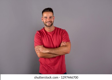 A Smiling Handsome Young Man In A Red Tshirt Standing In Front Of A Grey Background In The Studio.