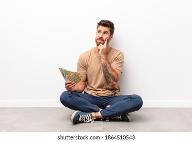 smiling happily and daydreaming or doubting, looking to the side holding dollar banknotes - Shutterstock ID 1864510543