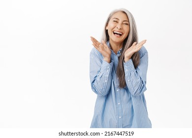 Smiling happy asian senior woman. Old japanese female with gray hair laughing and looking upbeat, standing over white background - Shutterstock ID 2167447519