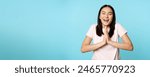 Smiling happy asian woman shows namaste, beg gesture and dreaming of something, making wish, high hopes, standing over blue background.