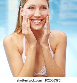 Smiling happy attractive woman putting sunscreen on her face