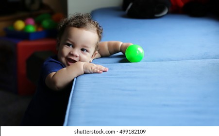 Smiling Happy Baby Leans On A Seat Cushion Playing With A Maraca Shaker.