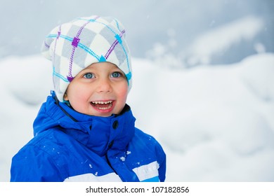 Smiling Happy Boy Having Fun Outdoors On Snowing Winter Day In Alps Playing In Snow.