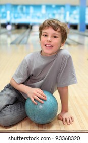 smiling happy boy sits on floor with blue ball in bowling club