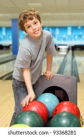 smiling happy boy stands near many colorful balls in bowling club