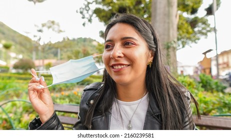 Smiling And Happy Brunette Latina Woman Holding Her Mask In Her Hand After The Quarantine And Covid-19 Is Over - No More Mask