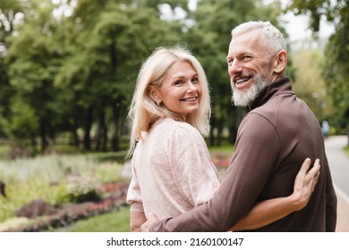 Smiling happy caucasian mature spouses hugging embracing while walking on a date in park together. Bonding, love and relationship