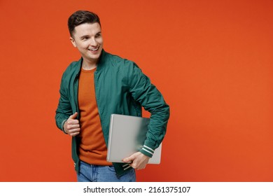 Smiling Happy Charming Fun Young Brunet Man 20s He Wear Red T-shirt Green Jacket Hold Use Work On Laptop Pc Computer Under His Hand Look Back Behind Isolated On Plain Orange Background Studio Portrait