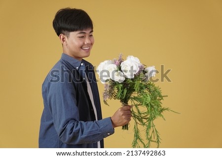 smiling happy cheerful young asian man dressed casually holding flower bouquet isolated on yellow studio background.