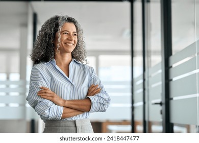 Smiling happy confident old mature professional business woman corporate leader, senior middle aged female executive, lady bank manager standing in office hallway arms crossed looking away, portrait. - Powered by Shutterstock