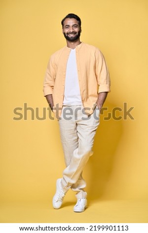 Smiling happy confident rich indian man standing isolated on yellow background. Happy handsome ethnic guy looking at camera advertising products posing for vertical full length portrait.