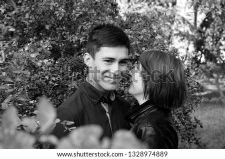 Smiling, happy couple in love, young man and woman in the park. The girl whispers in his ear guy. Black and white portrait of lovers