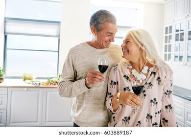 Smiling happy elderly couple enjoying retirement relaxing together in the kitchen drinking a glass of red wine, high key with copy space - Powered by Shutterstock