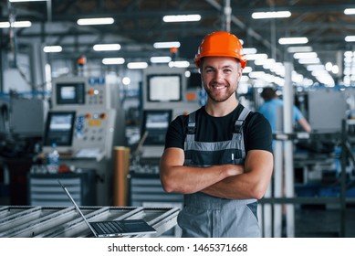 Smiling And Happy Employee. Industrial Worker Indoors In Factory. Young Technician With Orange Hard Hat.