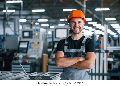 Smiling And Happy Employee. Industrial Worker Indoors In Factory. Young Technician With Orange Hard Hat.