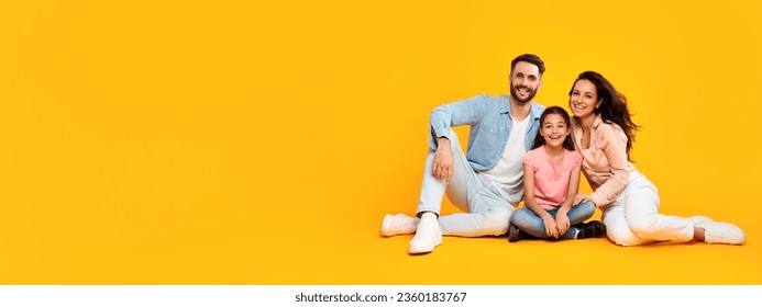 Smiling happy european parents sitting on the floor with their child girl, posing on yellow color background, panoramic shot, free copy space, banner - Shutterstock ID 2360183767