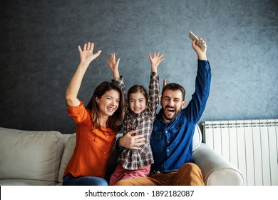 Smiling happy family sitting together on sofa and watching television. They are very excited and they holding hands in the air. - Shutterstock ID 1892182087