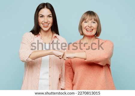 Smiling happy fun cool lovely elder parent mom with young adult daughter two women together wears casual clothes give fist bump lok camera isolated on plain blue cyan background. Family day concept