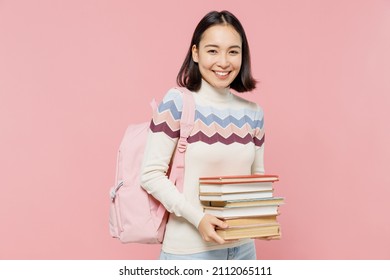 Smiling Happy Fun Teen Student Girl Of Asian Ethnicity Wearing Sweater Backpack Hold Pile Of Books Look Camera Isolated On Pastel Plain Light Pink Background Education In University College Concept