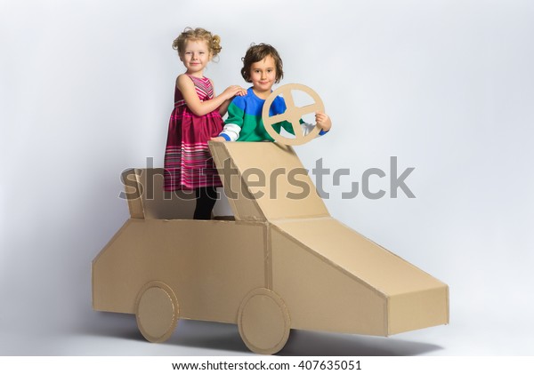 Smiling happy girl and boy near cardboard car.\
full length portrait