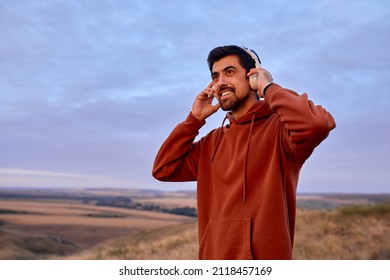 Smiling Happy Guy Is Wearing Modern Wireless Headphones Headset Before Training, Sportive Fit Male Listen To Music On Jogging, In The Morning At Sunrise. Jogging, Run, Sport, Fitness Concept