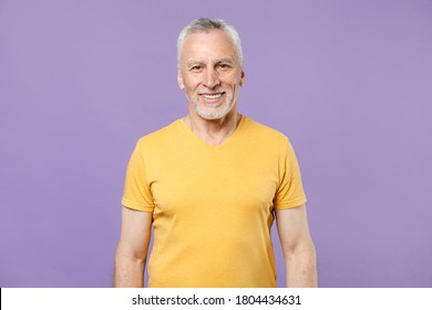 Smiling Happy Handsome Elderly Gray-haired Man 65 Years Old In Blank Basic Yellow T-shirt With Place For Logo Looking Camera Isolated On Pastel Violet Purple Background, Studio Portrait.