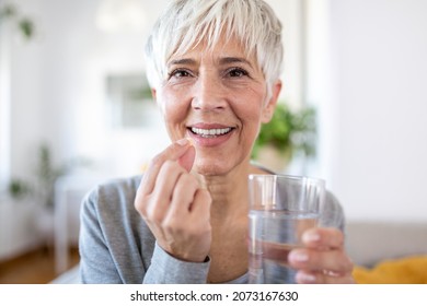 Smiling happy healthy middle aged 50s woman holding glass of water taking dietary supplement vitamin pill. Old women multivitamins antioxidants for anti age beauty. - Shutterstock ID 2073167630