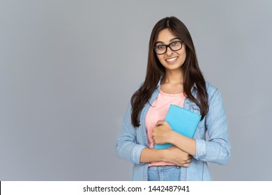 Smiling Happy Indian Young Woman College University School Student Wear Glasses Holding Book Isolated On Grey Studio Background, Positive Teen Girl Looking At Camera Stand With Copy Space, Portrait
