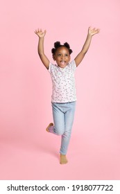 Smiling happy little african american kid girl 6-7 years old wearing casual clothes, standing with hands raised up, looking away and isolated on pink background. Childhood lifestyle concept