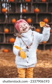 smiling happy little child girl in coat  holding autumn leaves, having fun in fall forest