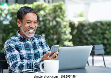 Smiling happy mature man with white stylish short beard using smartphone gadget serving internet at coffee shop cafe outdoor. Laughing old man using social media network technology feeling excited.