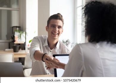 Smiling happy millennial man handshaking african female coworker celebrating successful teamwork, satisfied diverse colleagues shaking hands excited by good result, thanking for help support concept