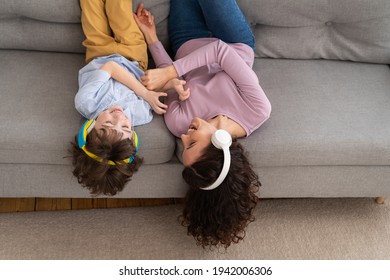 Smiling happy mother and kid son lying upside down on couch at home, laughing, tickling each other hearing songs in earphones. Playful child and mom wear headphones enjoy listening to music together. - Powered by Shutterstock