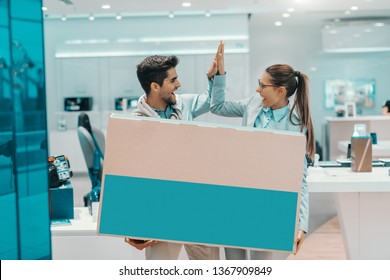 Smiling Happy Multicultural Couple Dressed Elegant Holding Box With New Plasma Tv And Giving High Five To Each Other While Standing In Tech Store.