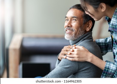 Smiling happy older asian father with stylish short beard touching daughter's hand on shoulder looking and talking together with love and care. Family relationship with bond and care concept.