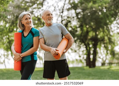 Smiling happy senior couple holding yoga mats smiling in park, talking together, looking away. Healthy lifestyle concept - Powered by Shutterstock